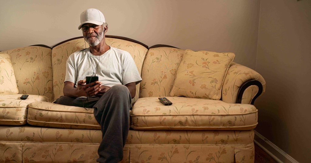 A black man uses his phone on a cream couch