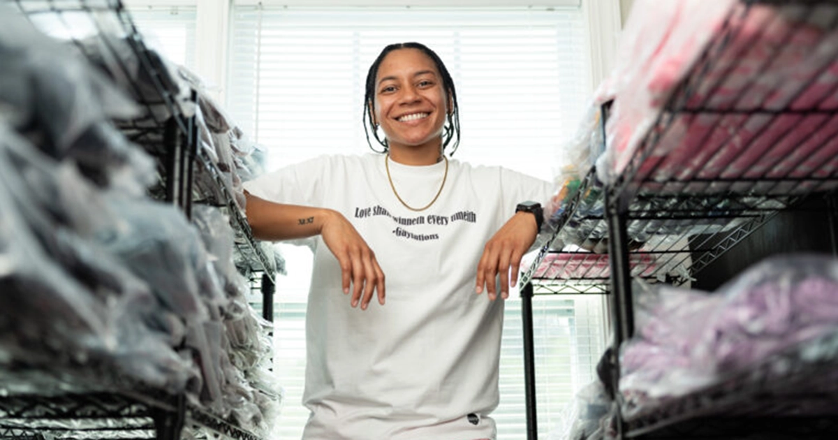A young black woman stands in between two shelves of T-shirts