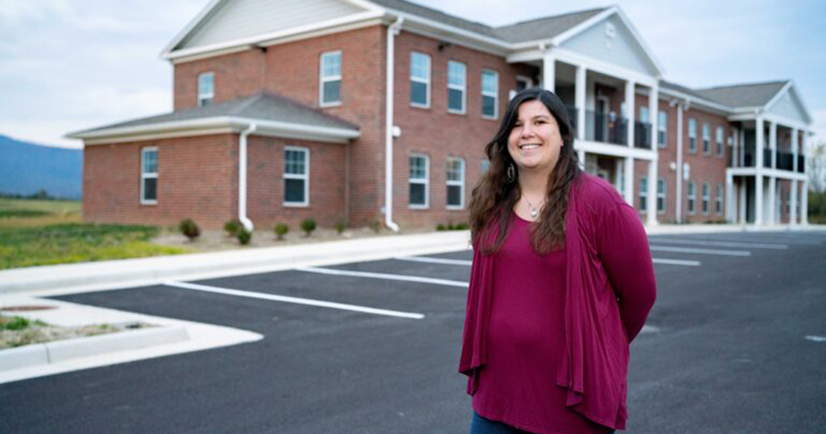A young woman stands in the parking lot of a brick apartment building