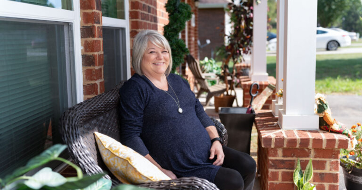 A middle-aged woman sits on the front porch of a brick building