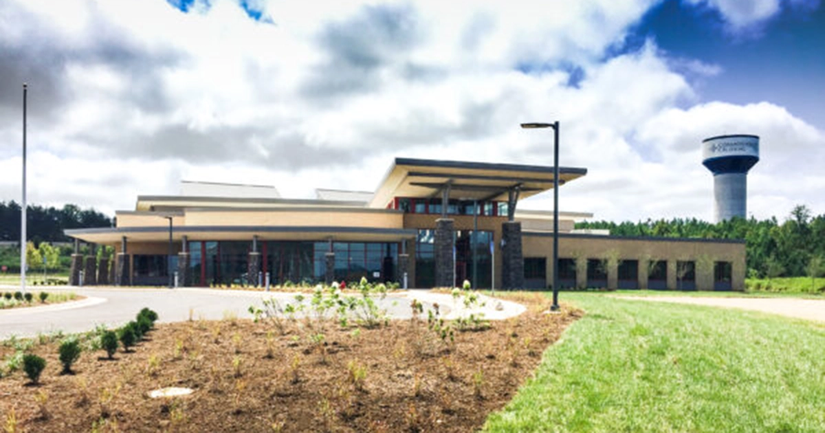 A large building with grass and brown dirt in front and a blue sky with white clouds
