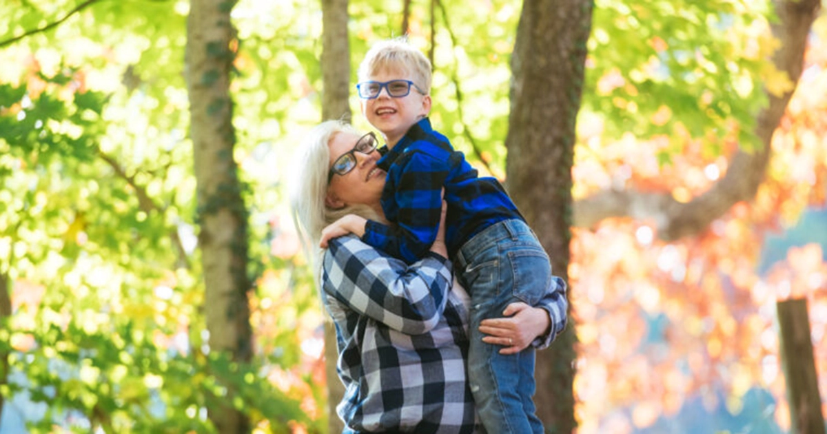 A woman holds a young boy in the woods