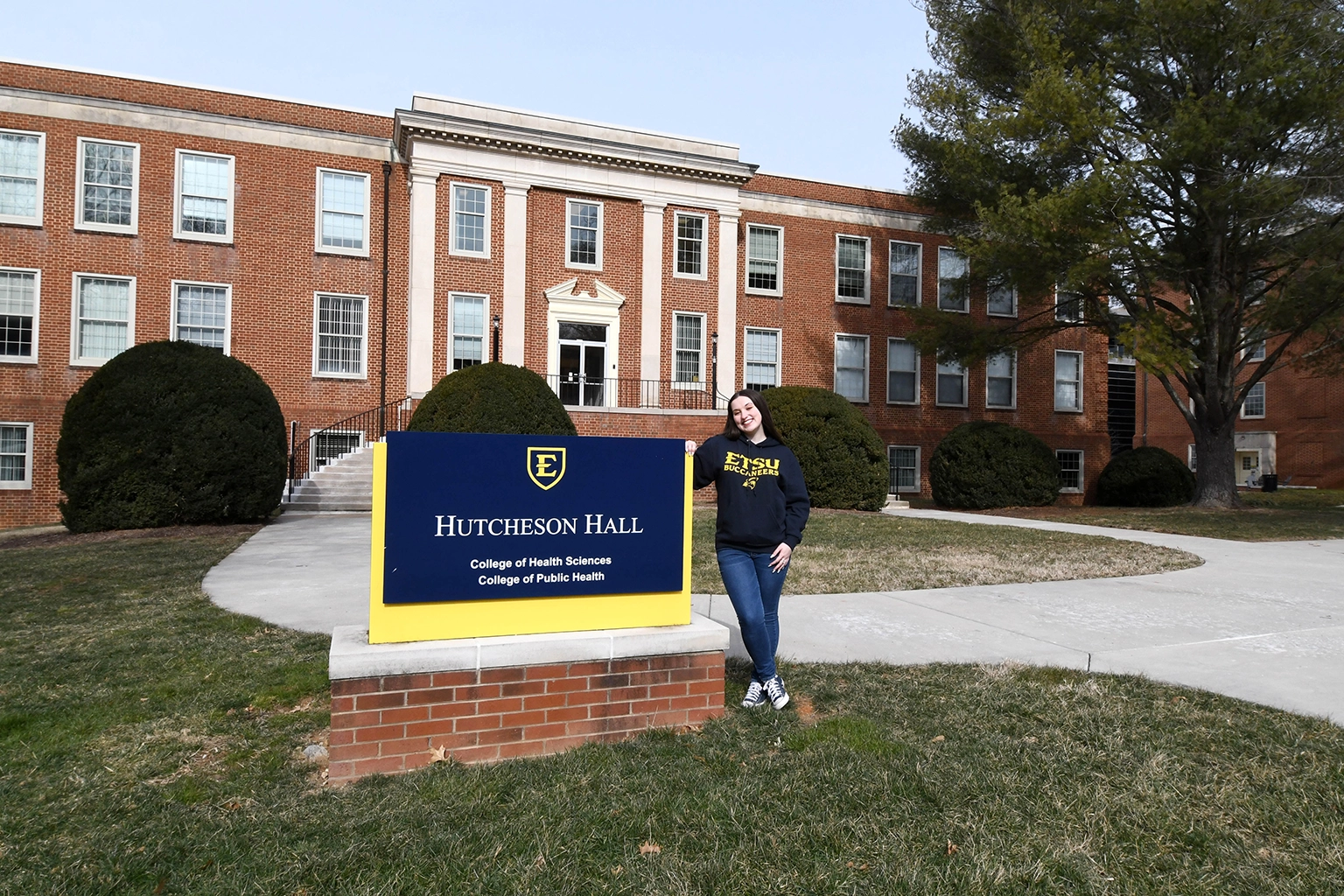 Laura Clifton stands beside the Hutcheson Hall sign at East Tennessee State University, home to the College of Health Sciences and College of Public Health.